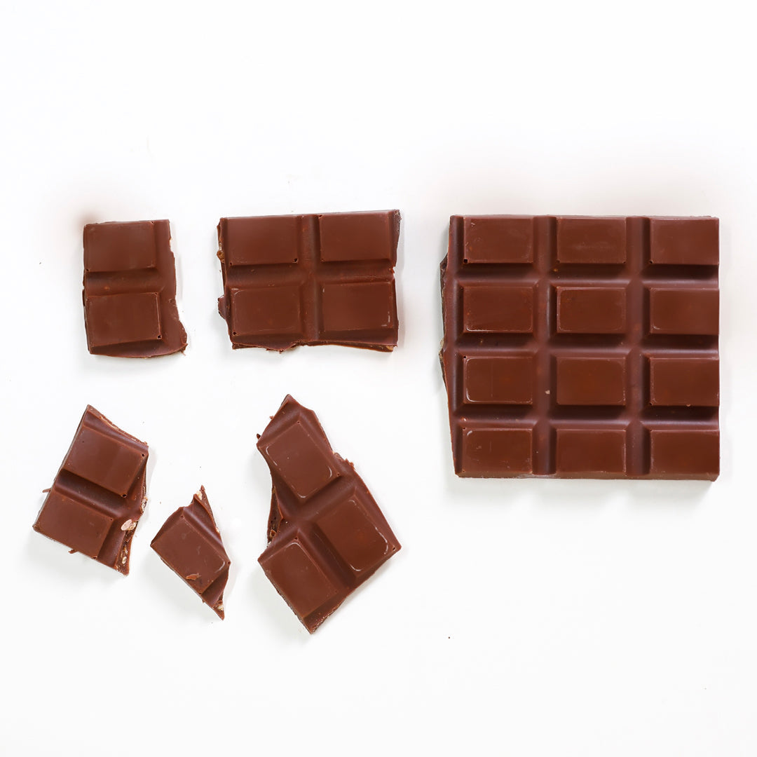Barra de chocolate artesanal com crispy de coco, dentro de embalagem, com quadrados de chocolate ao redor.