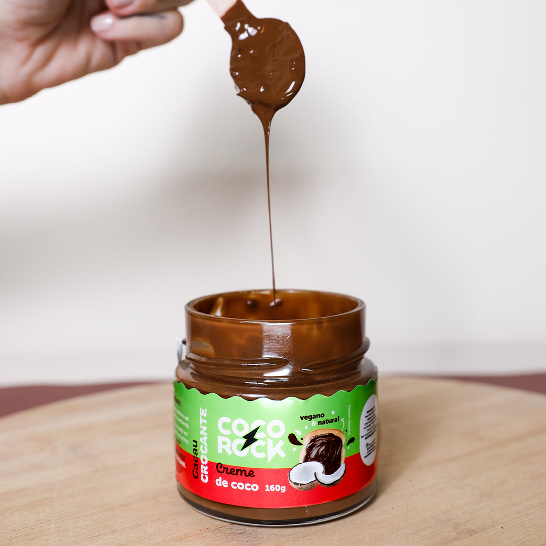 Colher com creme de coco cacau crocante escorrendo para dentro do pote do produto, mostrando cremosidade intensa.